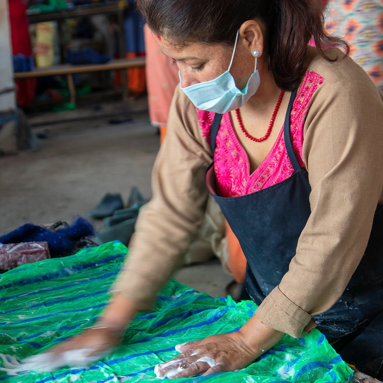 woman wearing apron and mask working at a wet felting table
