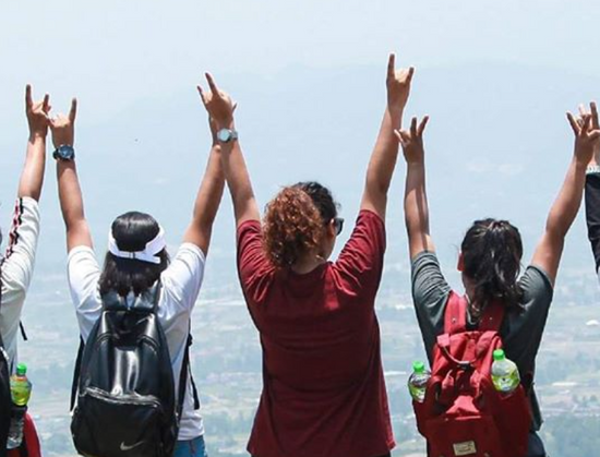 young women on the top of a mountain standing side by side looking out across a sweeping valley view with their arms outstretched overhead