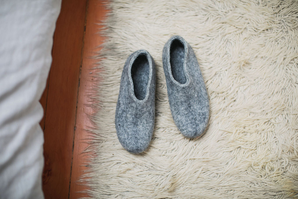 grey wool slippers sitting on a shaggy bedside rug