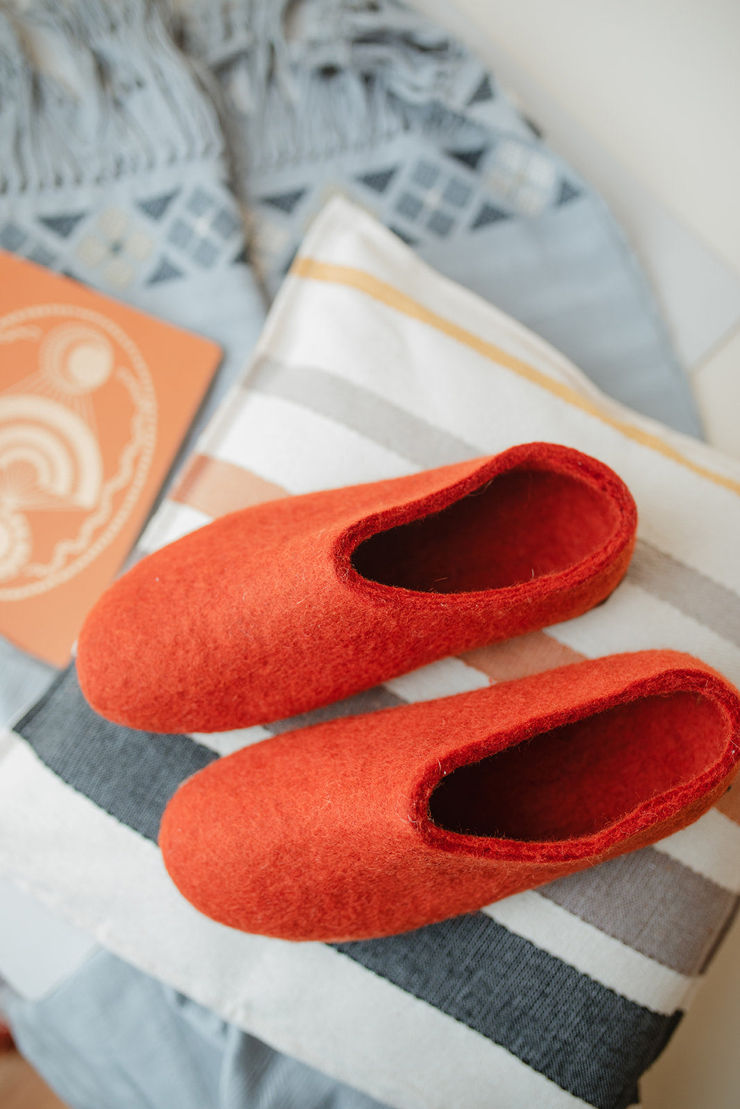 spice red wool slippers on top of a modern striped cotton throw pillow