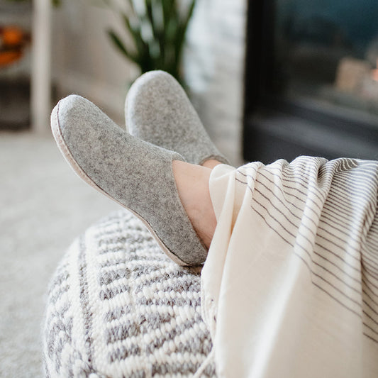 woman snuggled under a blanket wearing cozy wool felt slippers in grey