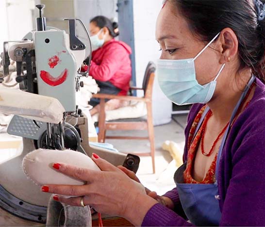 female artisan in a surgical mask stitching a leather sole onto a wool felt slipper